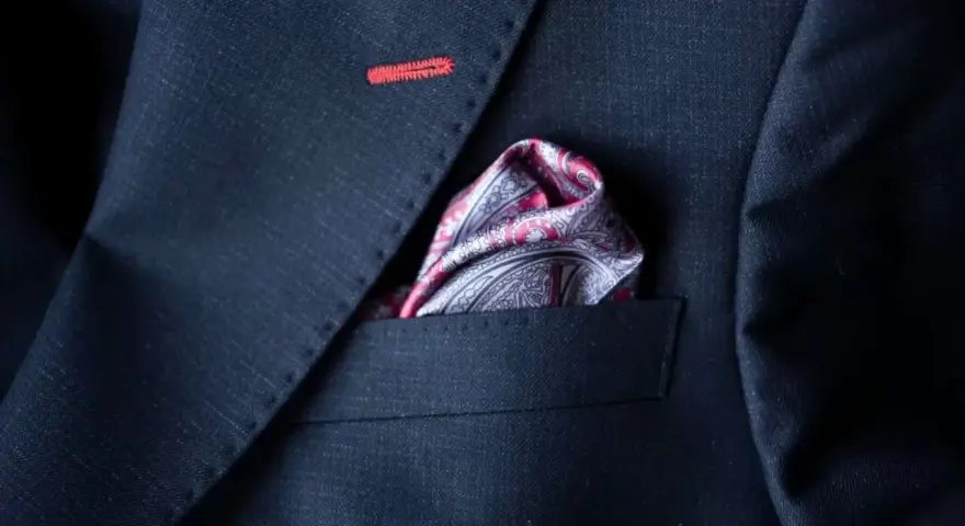 Elegancka poszetka w paisley do granatowego garnituru, z subtelnym czerwonym przeszyciem na klapie.