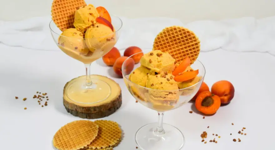 Zwei Gläser mit cremigem Aprikosen Eis, garniert mit frischen Aprikosenstücken und Waffeln. Ein sommerlicher Genuss!