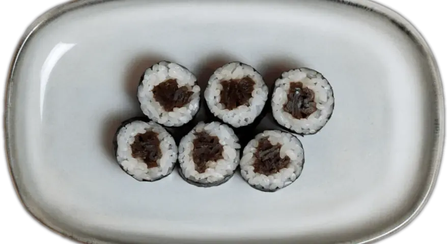 Sześć kawałków sushi z ryżem i ciemnym nadzieniem na szarej tacy.