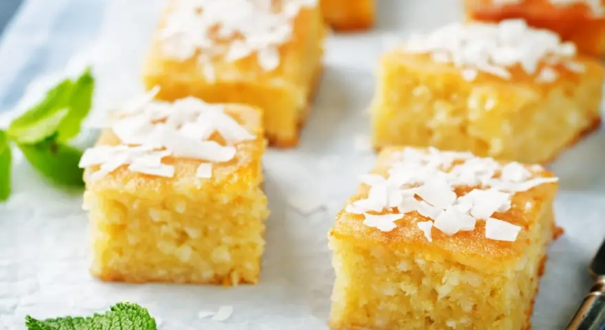 Fette di torta al cocco dorata, guarnite con scaglie di cocco e foglie di menta fresca.