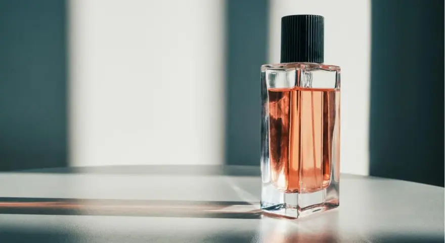 Eine Glasflasche mit rosafarbenem Parfum und schwarzem Deckel, beleuchtet von Sonnenlicht.
