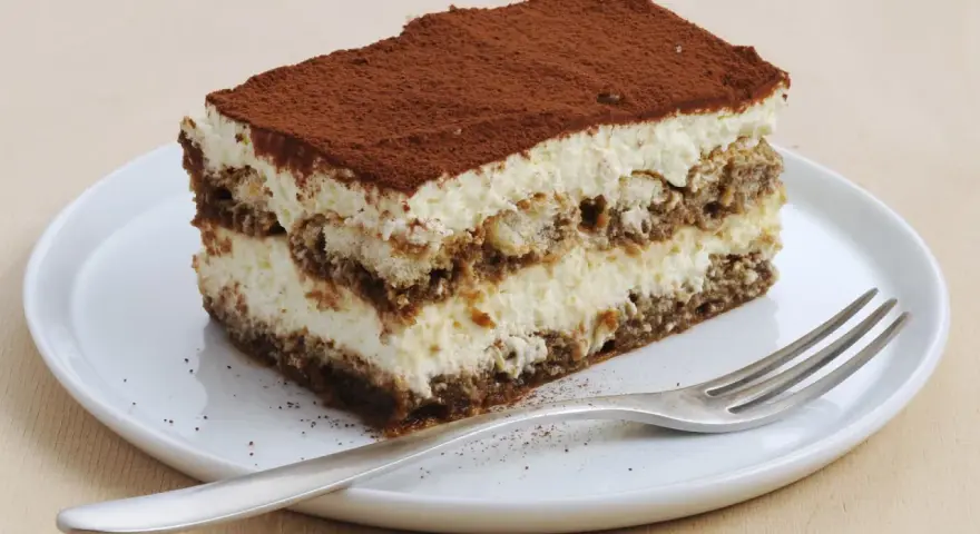 Une part de tiramisu sans oeuf, légère et aérienne, saupoudrée de cacao, sur une assiette blanche avec une fourchette.