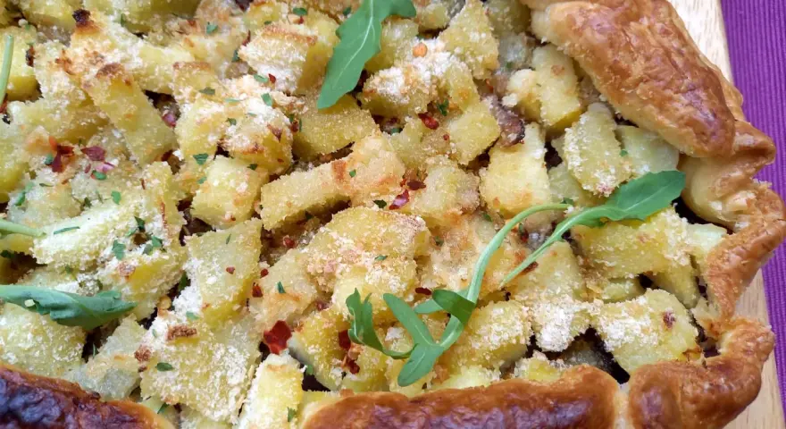 Torta salata patate e cipolle dorata e croccante, guarnita con rucola e peperoncino.