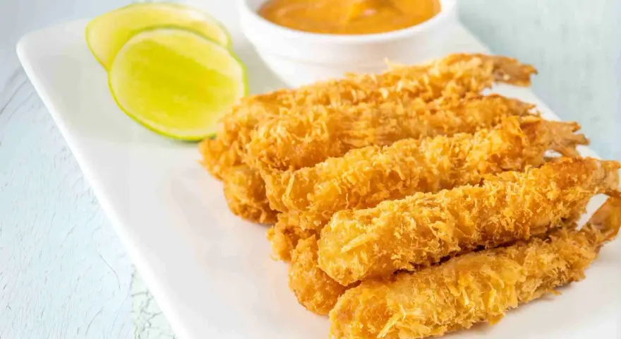 Crujientes gambas a la gabardina doradas, servidas con rodajas de lima y una salsa cremosa.
