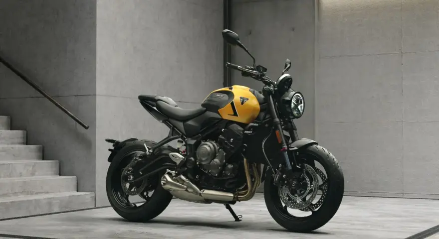Żółty motocykl Triumph Trident 660 z czarnymi akcentami stoi na betonowej posadzce obok schodów.