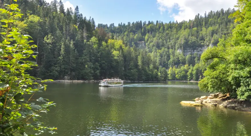 Bateau naviguant sur une rivière bordée de forêts luxuriantes, un paysage typique des chutes du Doubs.