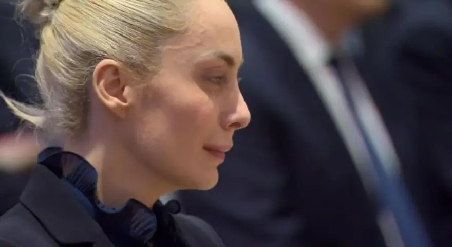 Marta Fascina, con i capelli raccolti, indossa un abito scuro. La sua espressione pensierosa suggerisce un momento di riflessione prima di un evento importante, forse legato a Silvio Berlusconi.