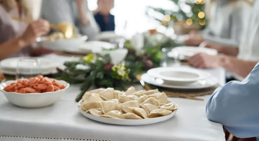 Talerz pierogów i miska z marchewką na wigilijnym stole, w tle rodzina i choinka.