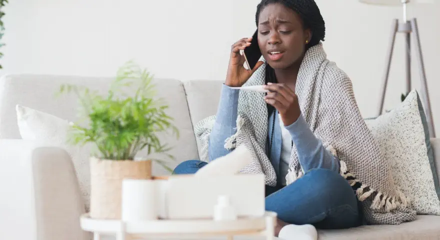 Femme malade au téléphone, thermomètre en main, elle doit se mettre en arrêt maladie avant entretien préalable licenciement.