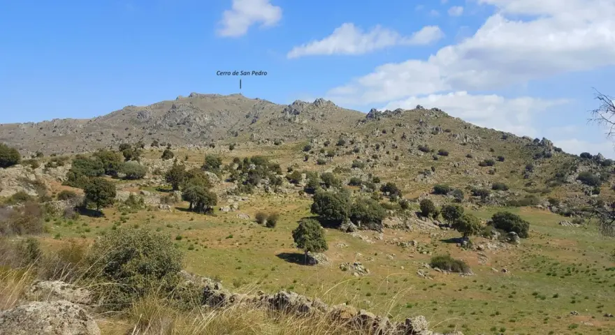 Paisaje rocoso y verde con el **cerro de San Pedro** en Colmenar Viejo al fondo.