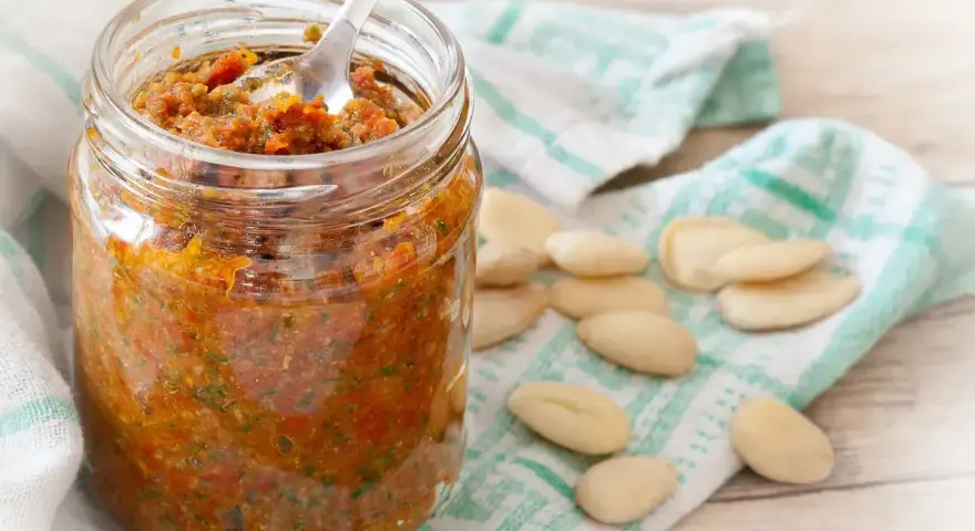 Vasetto di pesto di pomodori secchi, con mandorle sparse su un canovaccio.