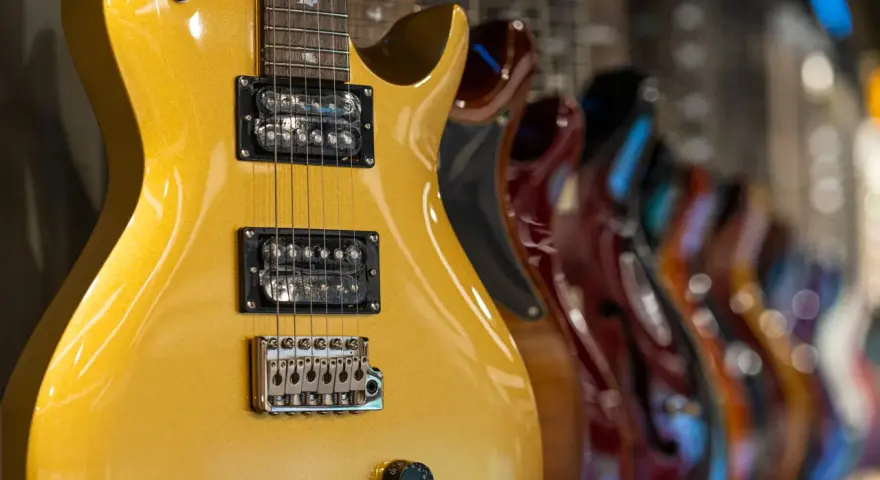 Guitarra eléctrica dorada con pastillas de **single coil** en primer plano, seguida de otras guitarras de colores.