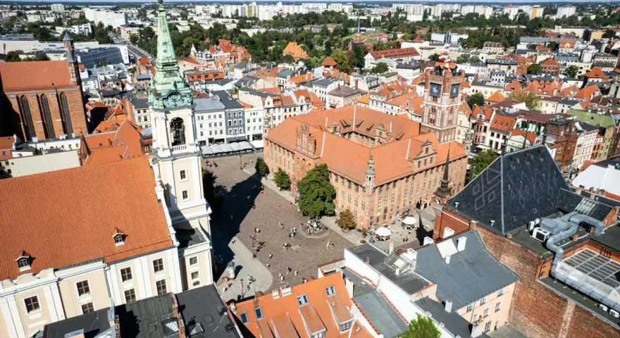 Widok na rynek i zabytkowe budynki Torunia, jednego z obiektów UNESCO w Polsce. Widać Ratusz Staromiejski i wieżę kościoła.