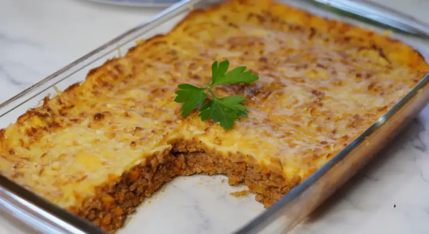 Pastel de papa recién horneado en refractario de vidrio, con una porción retirada, decorado con perejil fresco.