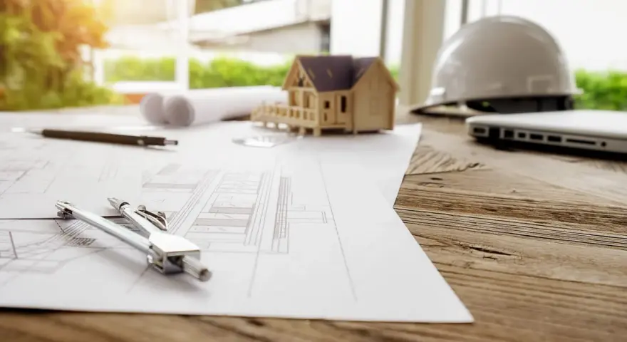 Plans, maquette de maison, casque et ordinateur sur un bureau en bois. La question est : combien de temps est valable un permis de construire ?