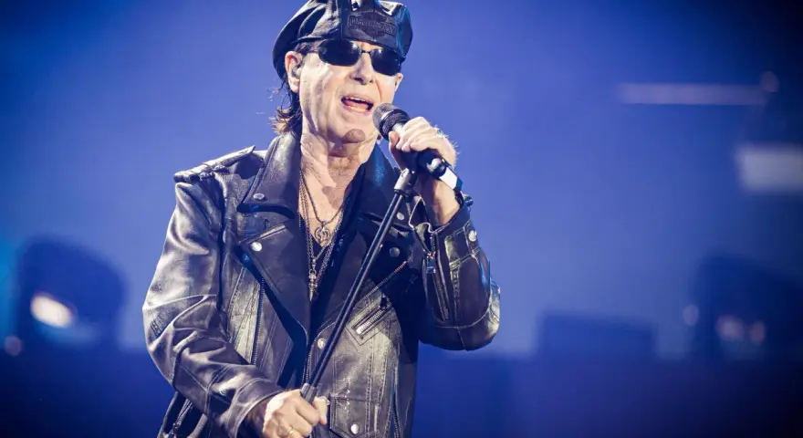 Klaus Meine, jung und rockig, singt ins Mikrofon, trägt Lederjacke und Kappe.