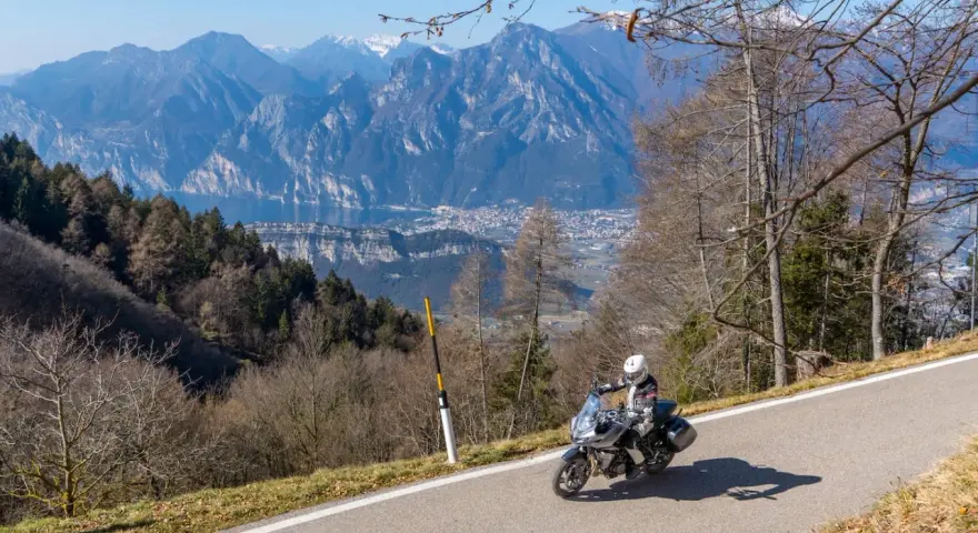 Motociclista in un panoramico motogiro Lombardia, con montagne maestose e un lago sullo sfondo.