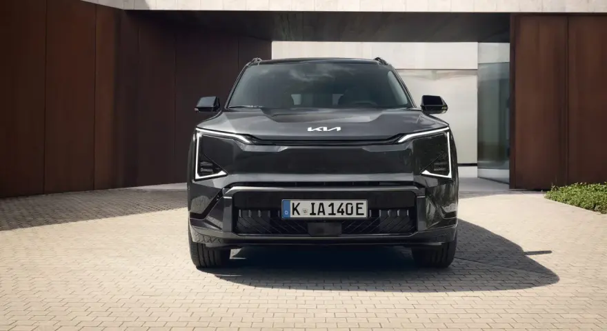 Szary SUV Kia EV5 z charakterystycznymi światłami LED, zaparkowany przed nowoczesnym budynkiem.