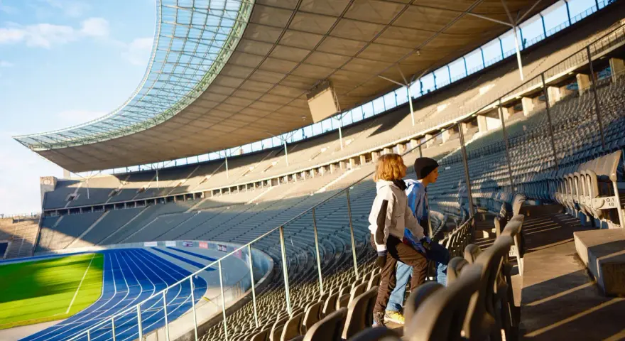 Zwei Kinder stehen auf den Rängen des Olympiastadion Berlin und blicken auf die Laufbahn.