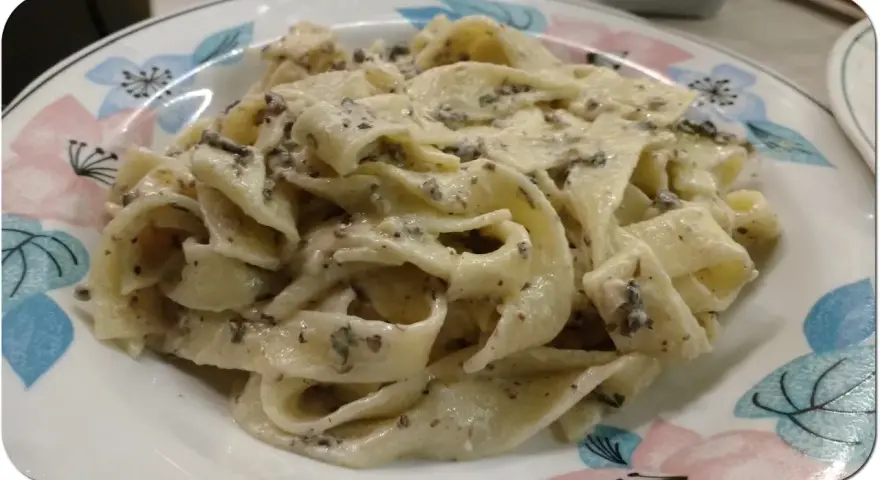 Pappardelle z kremowym sosem z mascarpone i aromatyczną pastą truflową, podane na talerzu z kwiatowym wzorem.
