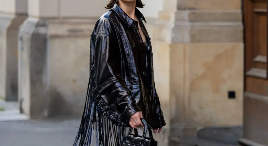Mujer con vestido negro y chaqueta de charol con flecos. Un look audaz para combinar vestido negro con chaqueta.