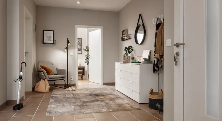 Stilvoller Flur gestalten: Grauer Sessel, Teppich, weiße Kommode mit Spiegel und Garderobe schaffen eine einladende Atmosphäre.