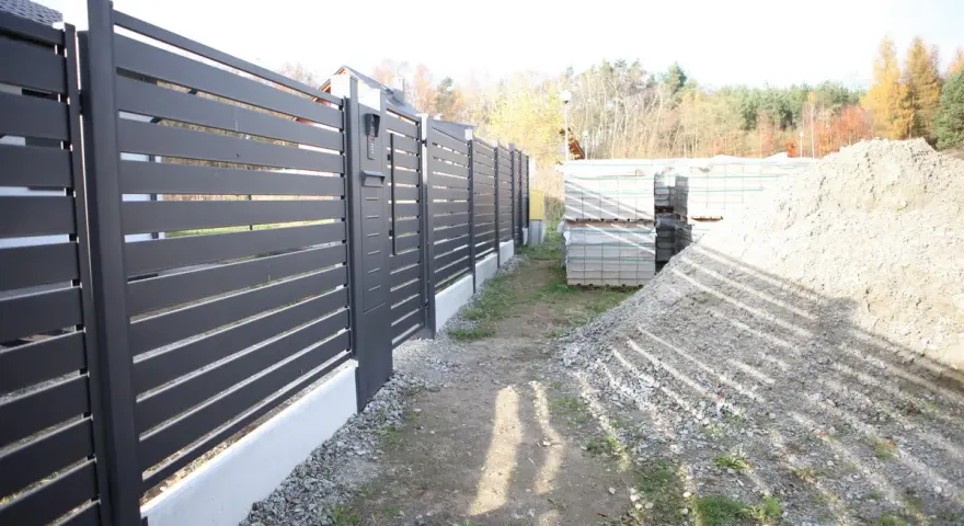Solidny fundament pod bramę przesuwną, gotowy na montaż nowoczesnego ogrodzenia. Obok materiały budowlane.