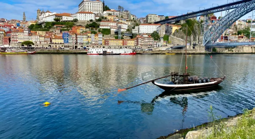 A traditional Rabelo boat with barrels, a symbol of Porto's wine heritage, floats on the Douro River. This iconic view is a must-see for any Porto travel guide.