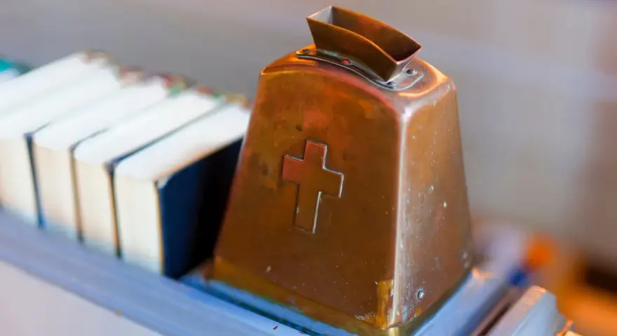Kupferne Klingel mit Kreuz, bereit für Spenden. Hier wird über Kirchensteuer Befreiung nachgedacht.
