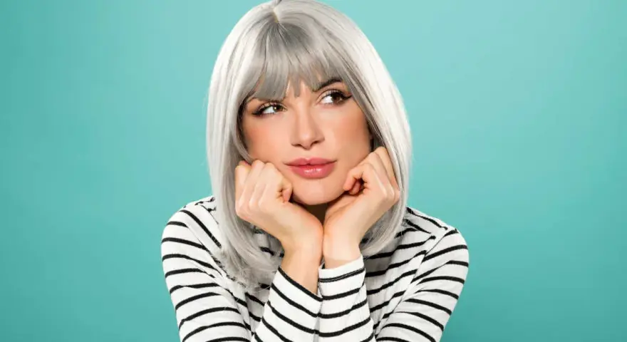 Donna con eleganti capelli grigi, appoggiata alle mani, con un'espressione sognante.