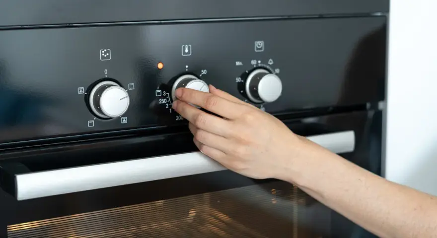 Hand dreht Temperaturregler am Ofen auf 250 Grad. Die Frage "wie lange Ofen vorheizen" wird durch das Einstellen der Temperatur beantwortet.