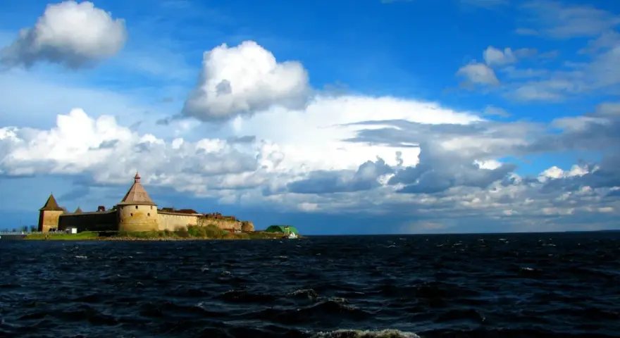 Forteca na wyspie nad największym jeziorem Europy, woda faluje pod błękitnym niebem z chmurami.