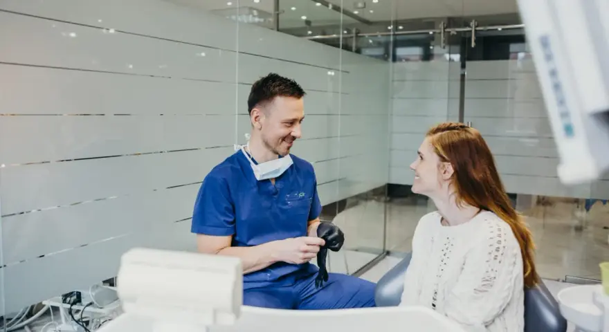 Dentysta w niebieskim uniformie rozmawia z pacjentką, sugerując nowy lek na ból zęba.