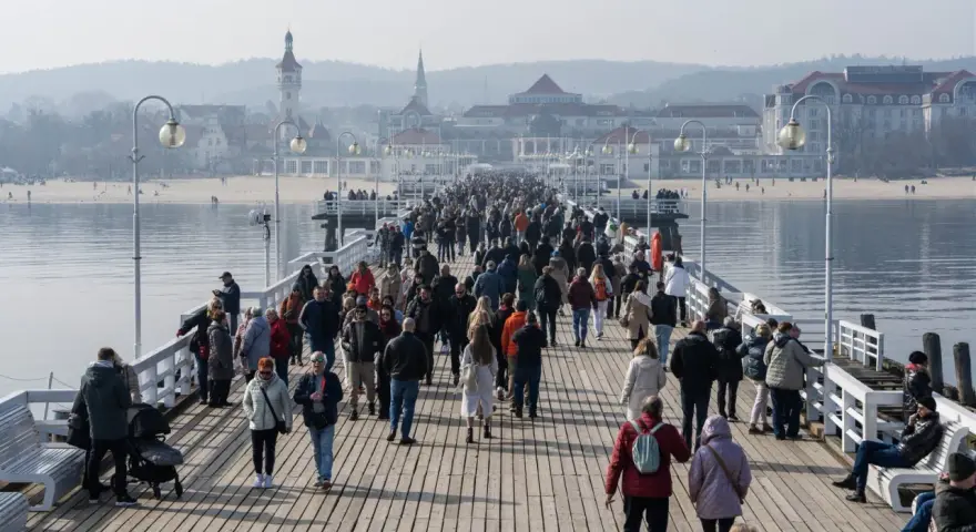 Tłumy ludzi spacerują po drewnianym molo w Sopocie. Czy molo w Sopocie jest płatne? Tego dnia wejście było darmowe, co przyciągnęło wielu turystów.