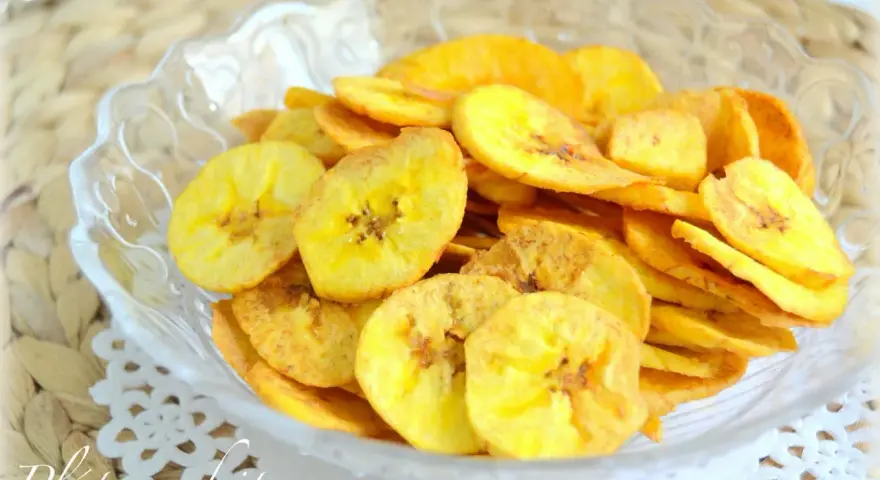 Crujientes rodajas de plátano frito doradas, servidas en un cuenco de cristal. Un delicioso snack casero.