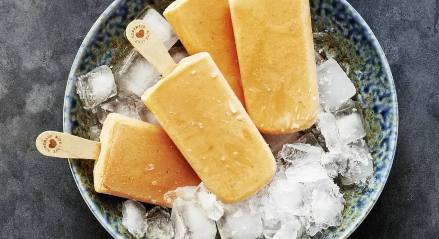 Vier selbstgemachte Papaya-Eis am Stiel liegen auf zerstoßenem Eis in einer blauen Schale.
