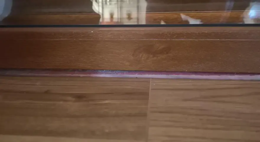 Drewniana listwa przy drzwiach balkonowych, z widoczną podłogą i fragmentem szyby.
