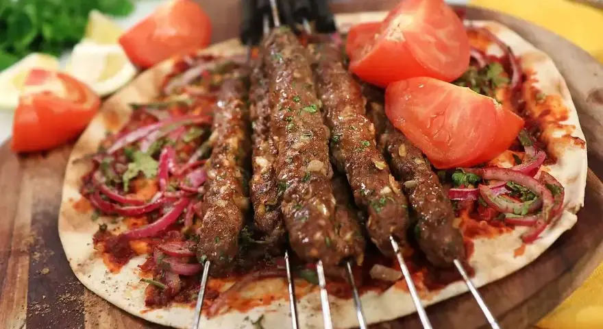 Grillade Adana kebabspett på en bädd av tunnbröd med rödlök, tomat och persilja. Ett perfekt adana kebab recept för en smakrik måltid.