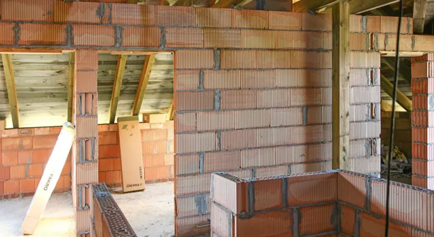 Budowa domu z pustaków ceramicznych. Widać niedokończone ściany, belki stropowe i materiały budowlane. Murowanie na piankę wady mogą pojawić się przy nieprawidłowym wykonaniu.