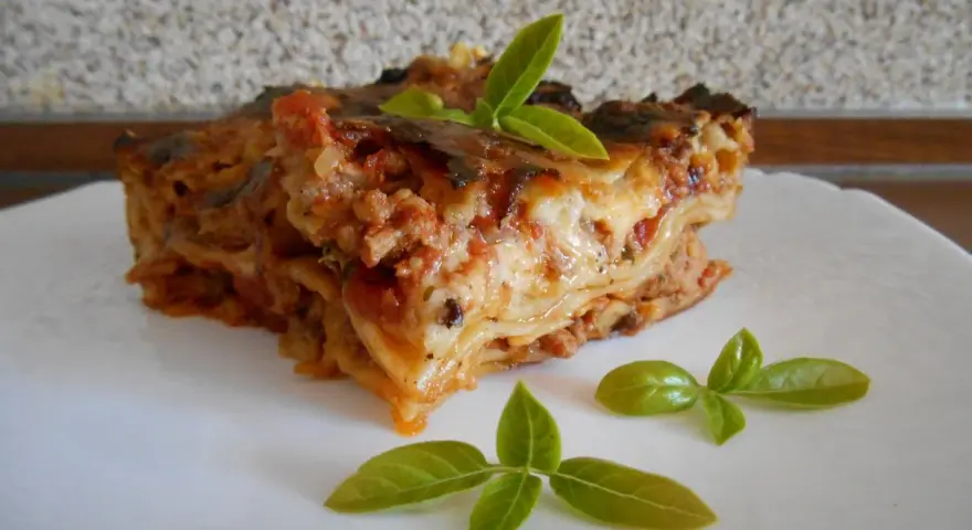 Kawałek pysznej lasagne z mięsem mielonym, udekorowany listkami bazylii. Prosty przepis na domową lasagne.