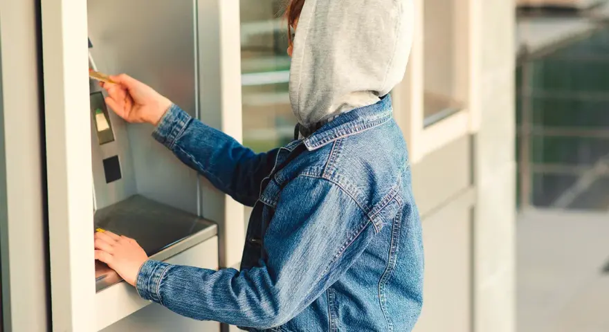 Jugendlicher mit Kapuze und Jeansjacke am Geldautomaten. Ein Beispiel für mögliche Verhaltensauffälligkeiten, die auf Kleptomanie bei Kindern hindeuten könnten.