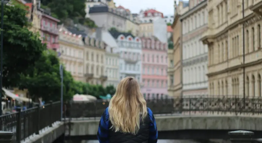 A woman with blonde hair gazes at colorful buildings, perhaps planning her day trips from Prague by train.