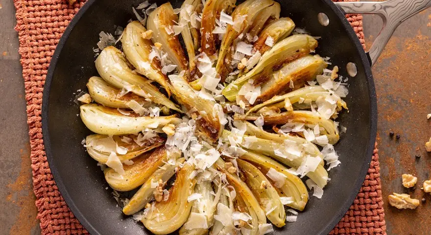 Finocchi in padella dorati e saporiti, guarniti con scaglie di formaggio e noci croccanti.