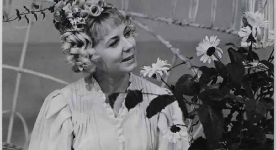 Ilona Stawińska w kwiecistej fryzurze i jasnej sukni, otoczona kwiatami, wygląda jak z baśni.