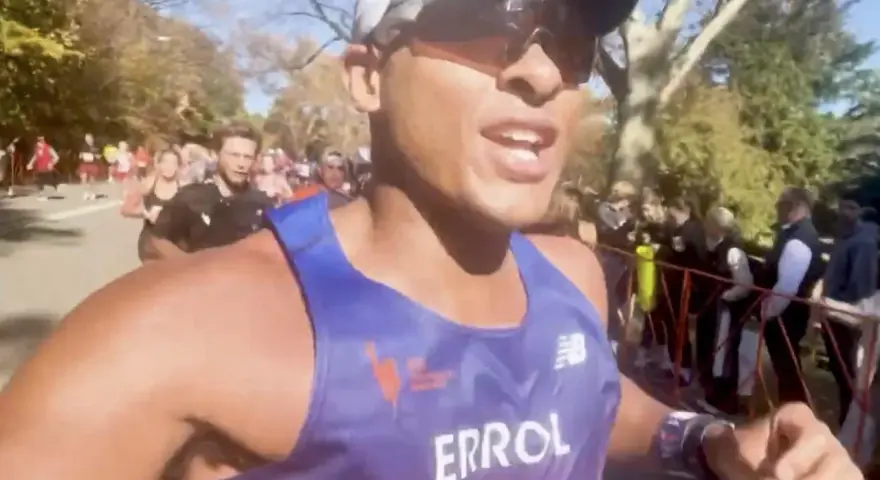 En löpare i blått linne, med texten "ERROL", kämpar på för att springa marathon. Publiken hejar längs banan.