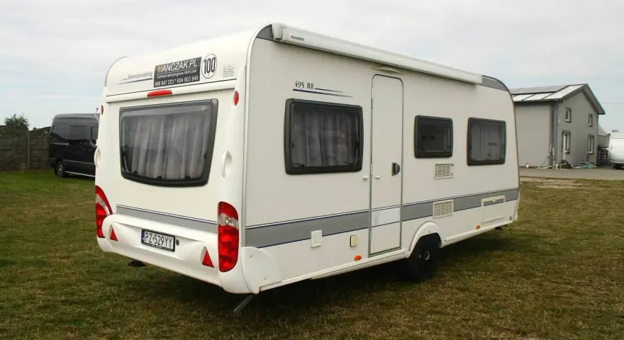 Biała przyczepa kempingowa Caravelair 495 RE na trawie, z widocznym logo MANCZAK.PL.
