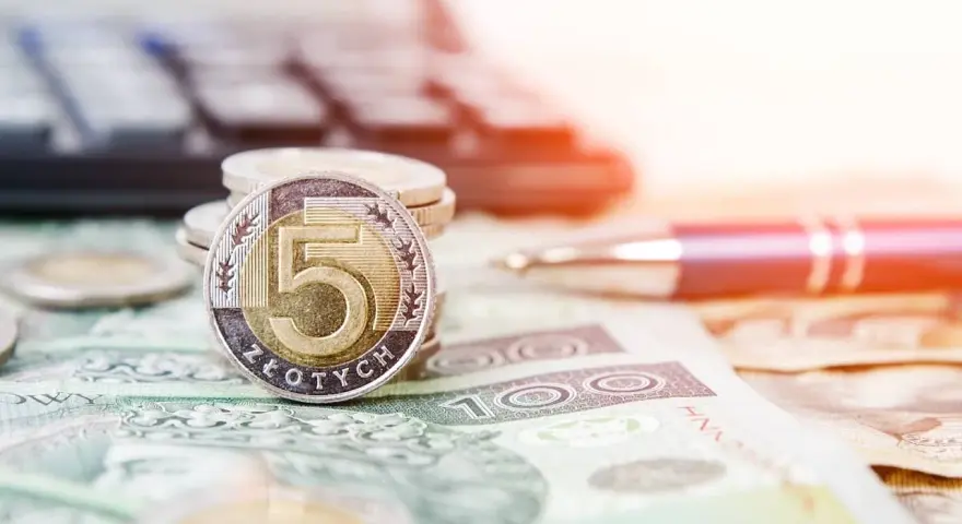 Złota moneta 5 złotych na stosie monet i banknotów. Obok długopis i kalkulator, sugerujące planowanie finansowe i możliwość recoverso rmc.