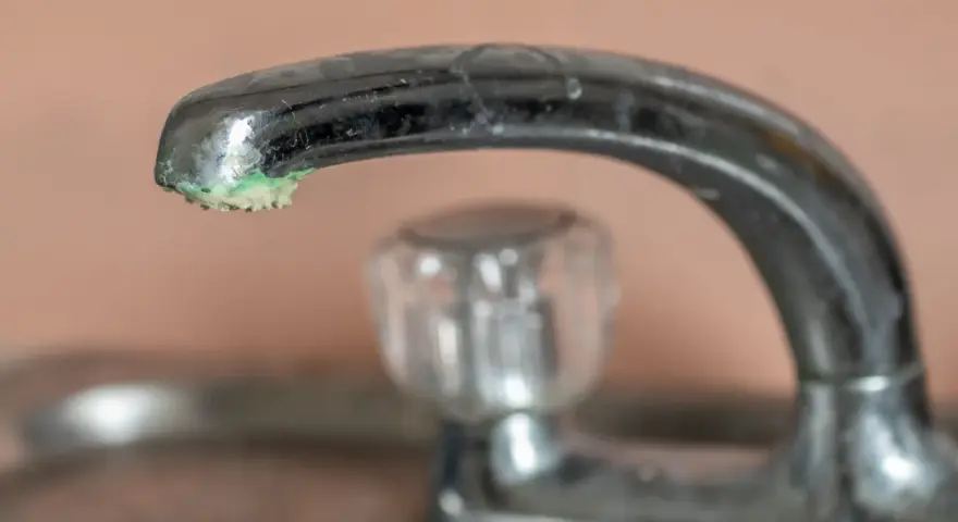 Robinet chromé avec un dépôt de calcaire vert de gris à son extrémité.