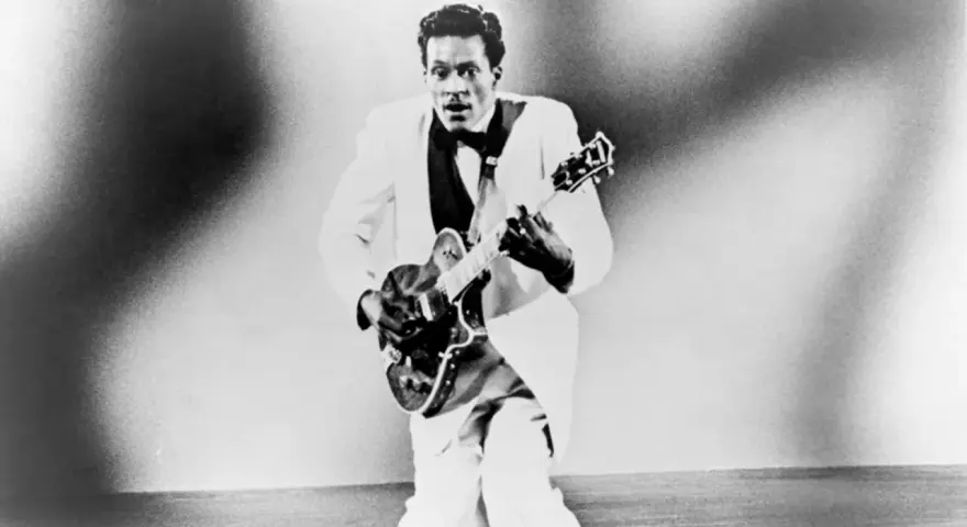 Chuck Berry in weißem Anzug spielt Gitarre, bereit für "Johnny B. Goode".