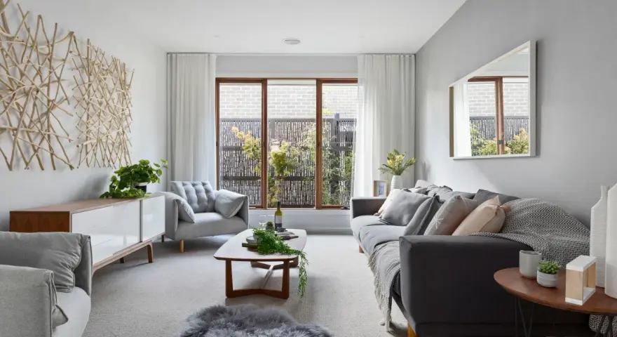 Sofá gris y sillón gris claro, con mesa de centro de madera. La decoración de ramas en la pared y la alfombra de piel gris crean un ambiente acogedor donde el beige y gris combinan a la perfección.